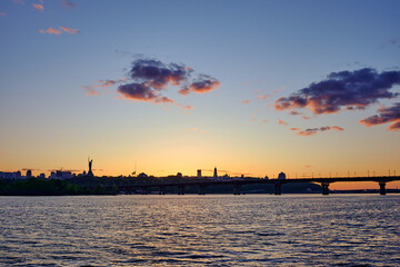 Beautiful sunset over Kyiv city skyline with Dnipro River, Paton Bridge, and Motherland Monument silhouette under colorful sky