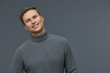Fototapeta premium Casual portrait of smiling man in gray turtleneck sweater looking at camera isolated on gray background with friendly expression, daytime, studio shot, people lifestyle concept.