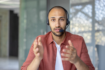 A man wearing a headset gestures while looking directly at the camera. He seems to be in a video...