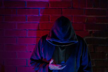Hoodie wearing a smartphone in front of a brick wall with spectacular lighting
