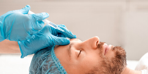 Middle aged man visiting aesthetic clinic, getting beauty injection, side view. Bearded man in hair...