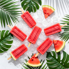 Juicy red popsicles on crushed ice with tropical leaves, flat lay on turquoise background – vibrant summer vibe.