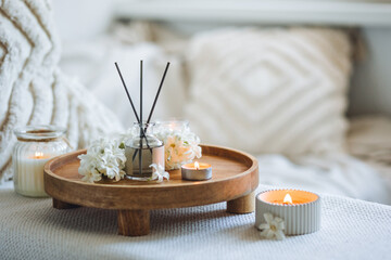 Aroma diffuser, burning candle, blooming hyacinth flowers and perfume on wooden bamboo tray. Cozy...