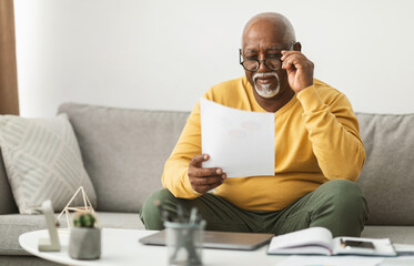 Senior African American Male Working With Papers Wearing Eyeglasses Sitting On Couch At Home....