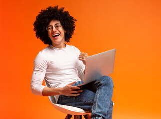 Modern job lifestyle. Young african-american man sitting on chair and working on laptop online,...
