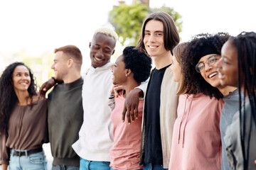 International group of friends in casual outfits smiling and embracing on the street, carefree...