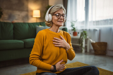 Mature blonde woman practice guided meditation manifestation at home - obrazy, fototapety, plakaty