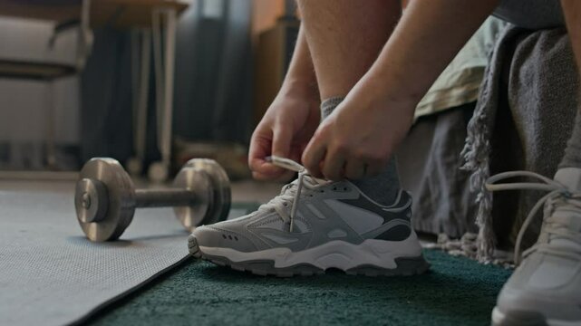 Medium close up of unrecognizable male hands tying shoelaces and standing up to start workout