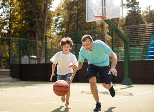 Portrait in action of father and son playing basketball on court together, man leading the ball