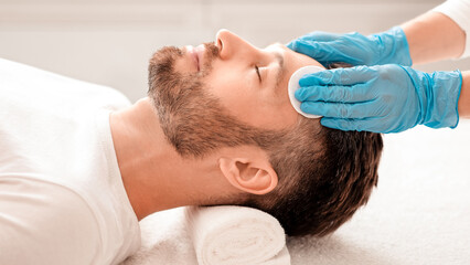 Middle aged handsome man attending cosmetologist, male face care concept. Side view of...