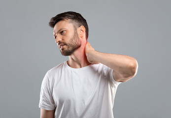 Obraz premium Tired middle aged man touching inflammated zone on his neck, having office syndrome, grey studio background, copy space. Man suffering from cervical osteochondrosis, rubbing lightened with red neck
