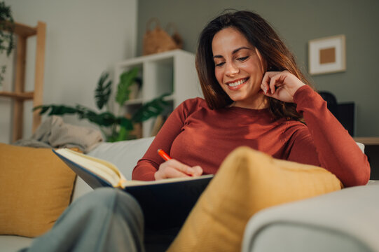 Happy woman writing on notebook sitting on sofa at home