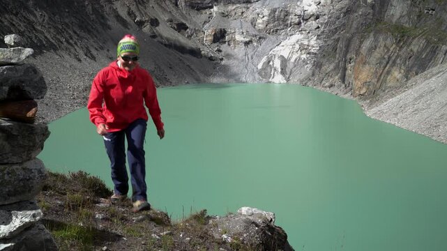 Smiling Female trekker dressed bright red jacket acclimatization round walking along high altitude Sabai Tso glacial lake cca 4350m. Makalu Barun National Park, Mera peak climbing route, Nepal
