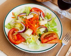 Colorful salad of chopped fresh lettuce with ripe tomatoes, sliced purple onion, carrot and white asparagus