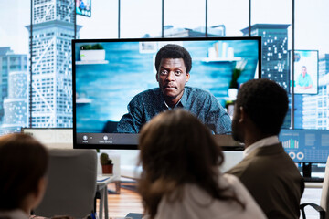Employees attending an online remote videocall meeting with general manager, presenting project updates for efficiency. Work team ensuring strategic goals achievement in a boardroom.