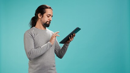 Portrait of upbeat person mindlessly scrolling on tablet screen, isolated over studio background. Cheerful man passing time on social media on portable device, enjoying leisure time, camera B © DC Studio