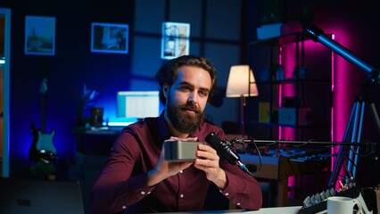 Man doing technology review of wireless portable speaker for internet vlogging channel. Music playing device held by content creator showing it to his subscribers, camera B