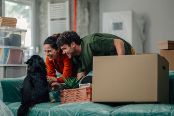 Happy couple unpacking boxes and playing with their dog in new home