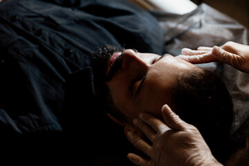 Stylish bearded man receiving facial massage in beauty salon