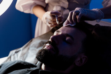 An attractive man receives mesotherapy injections to treat hair loss at the clinic. Injections into...