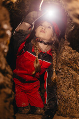 A 6-year-old girl in a protective suit and helmet with a flashlight in the middle of a natural...