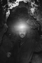 a young caving instructor dressed in a protective suit and helmet shows the route in a cramped gypsum cave