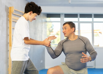 Adult man and boy teenager training self-defense techniques in studio