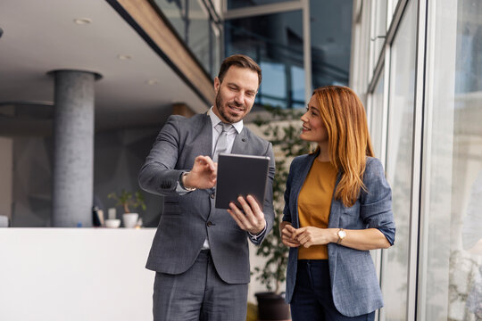 Businessman standing with his female colleague at enterprise and scrolling on tablet.