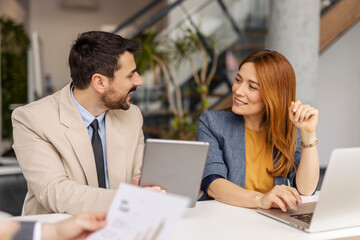 Two exerts discussing data on tablet and smiling at each other during the meeting at boardroom.