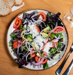 Diet salad consisting of pieces of tomato, avocado, cut onion and cheese dished up in a plate