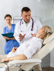 Male doctor and female assistant having conversation with elderly woman patient about need for...