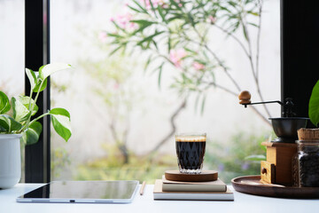 Coffee glass cup and tablet, notebook, cozy interior workspace by the window