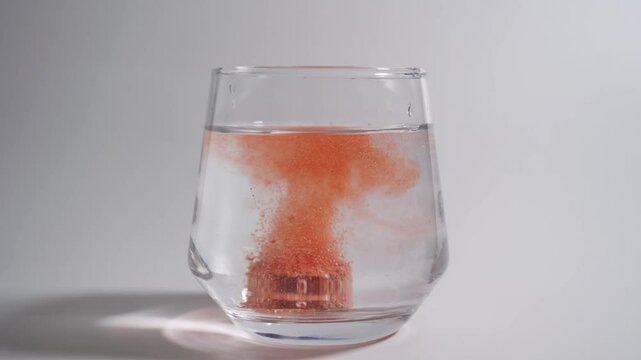 Effervescent tablets dropping into a glass of water slow motion on white background
