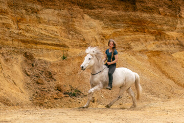 A young woman and her white icelandic horse gelding interacting in a sand pit; horsemanship concept