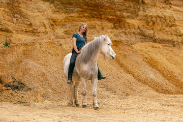 A young woman and her white icelandic horse gelding interacting in a sand pit; horsemanship concept