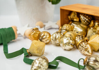 Small Gold Christmas Ornaments on a Green Ribbon with Wooden Box of Ornaments in Background