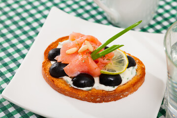 Close up image of canape with salmon and olives dressed with white sauce