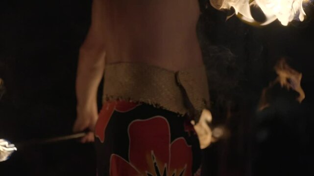 A striking close-up of a Polynesian fire dancer standing confidently with flaming torches held at his sides. Set against a deep night sky, the firelight illuminates the performer&rsquo;s form.