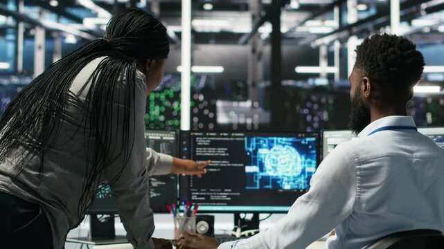 Manager supervising data center engineer using AI neural network models to configure hardware. Team leader overseeing employee using machine learning programming language to optimize systems, camera B
