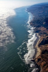 Spectacular aerial view showcases the meeting of ocean, coastline, and a layer of clouds.