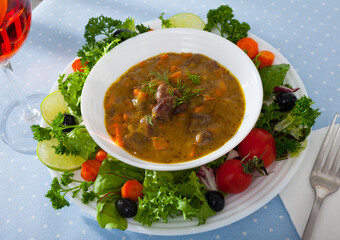 Image of goulash from chicken hearts with vegetables and fresh lettuce served at plate