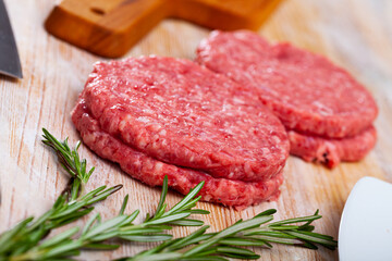 Uncooked meat cutlets for hamburgers with rosemary on wooden table