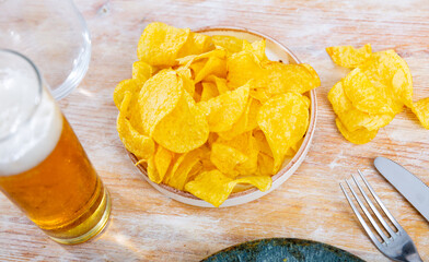 Plate with crunchy potato chips served with glass of beer