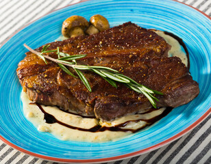 Fried beef loin decorated with rosemary served with grilled mushrooms and sauce on striped background