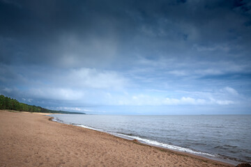 Wide, empty strand of honey-brown sand on the Baltic Sea under dramatic summer clouds at Saulkrasti beach (Saulkrastu Pludmale), a peaceful Vidzeme coast resort in Latvia in the baltic states.
