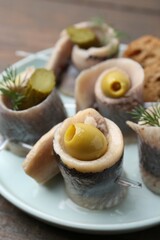 Delicious herring rolls with olives, pickles and dill on table, closeup