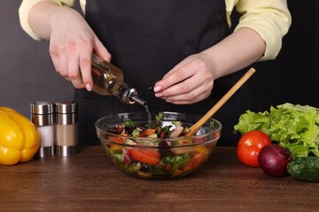 Woman pouring oil onto tasty salad at wooden table against dark background, closeup