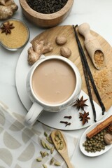 Aromatic Masala tea in cup, brown sugar, dry leaves and spices on white marble table, flat lay