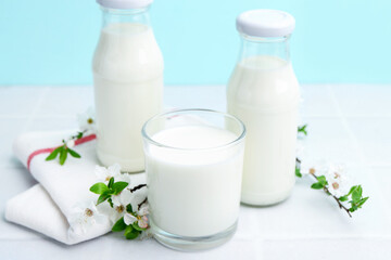 Fresh milk and blossoms on white table against light blue background
