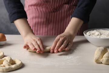 Woman making pretzel at white wooden table, closeup